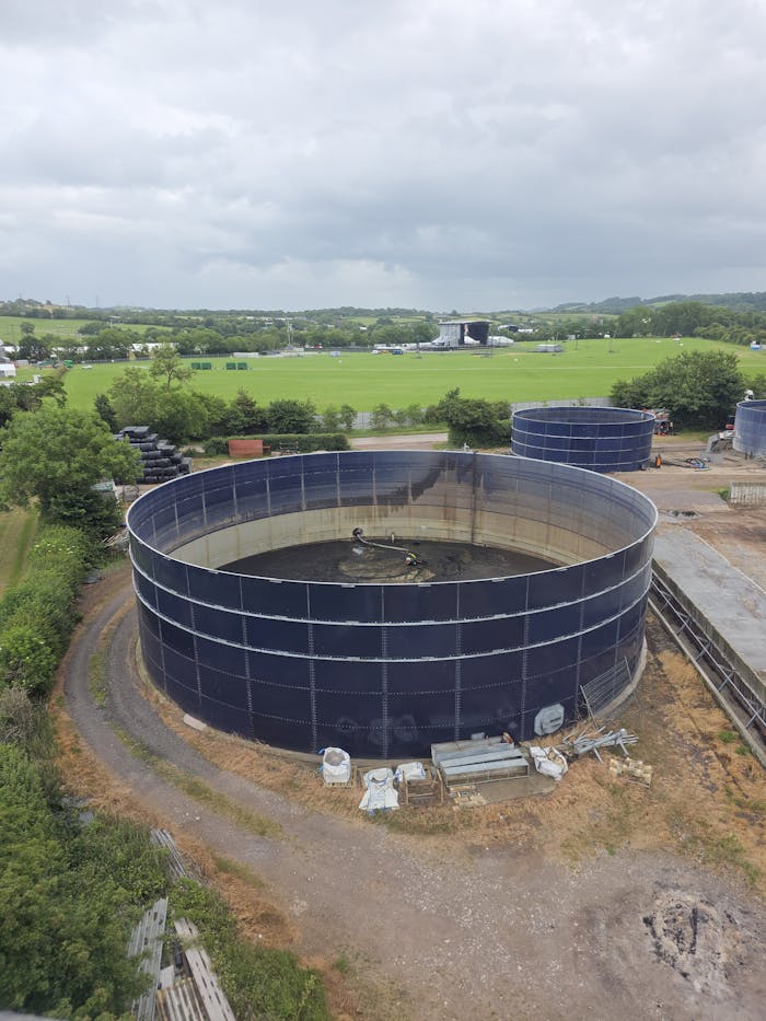 Aerial view of large circular water tanks at an industrial site amidst rural fields.